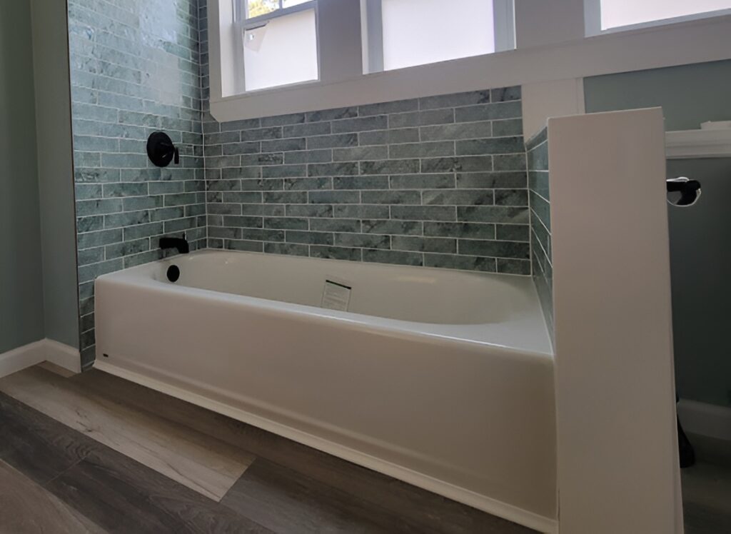 White alcove bathtub with green tile surround, black fixtures and three windows