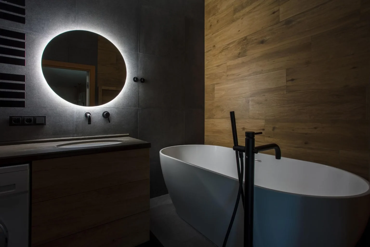 Freestanding tub beside dark vanity and wood-look wall tile