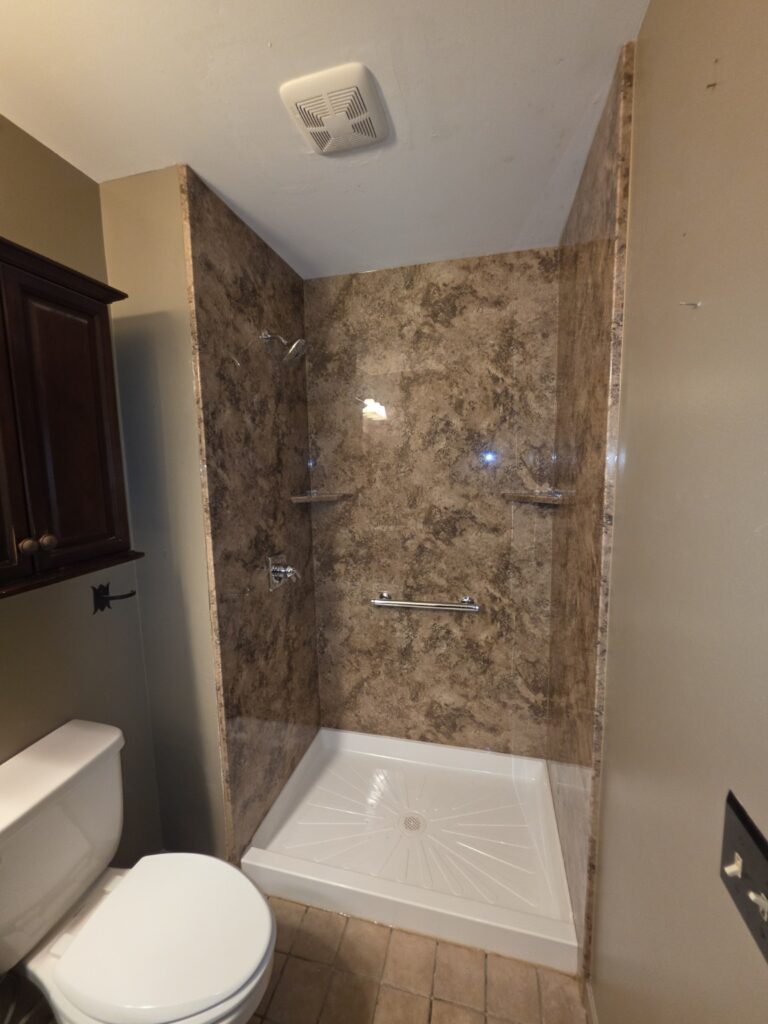 Delmar Madeira Granite-pattern acrylic shower with white base, corner shelves and grab bar, before glass-door installation